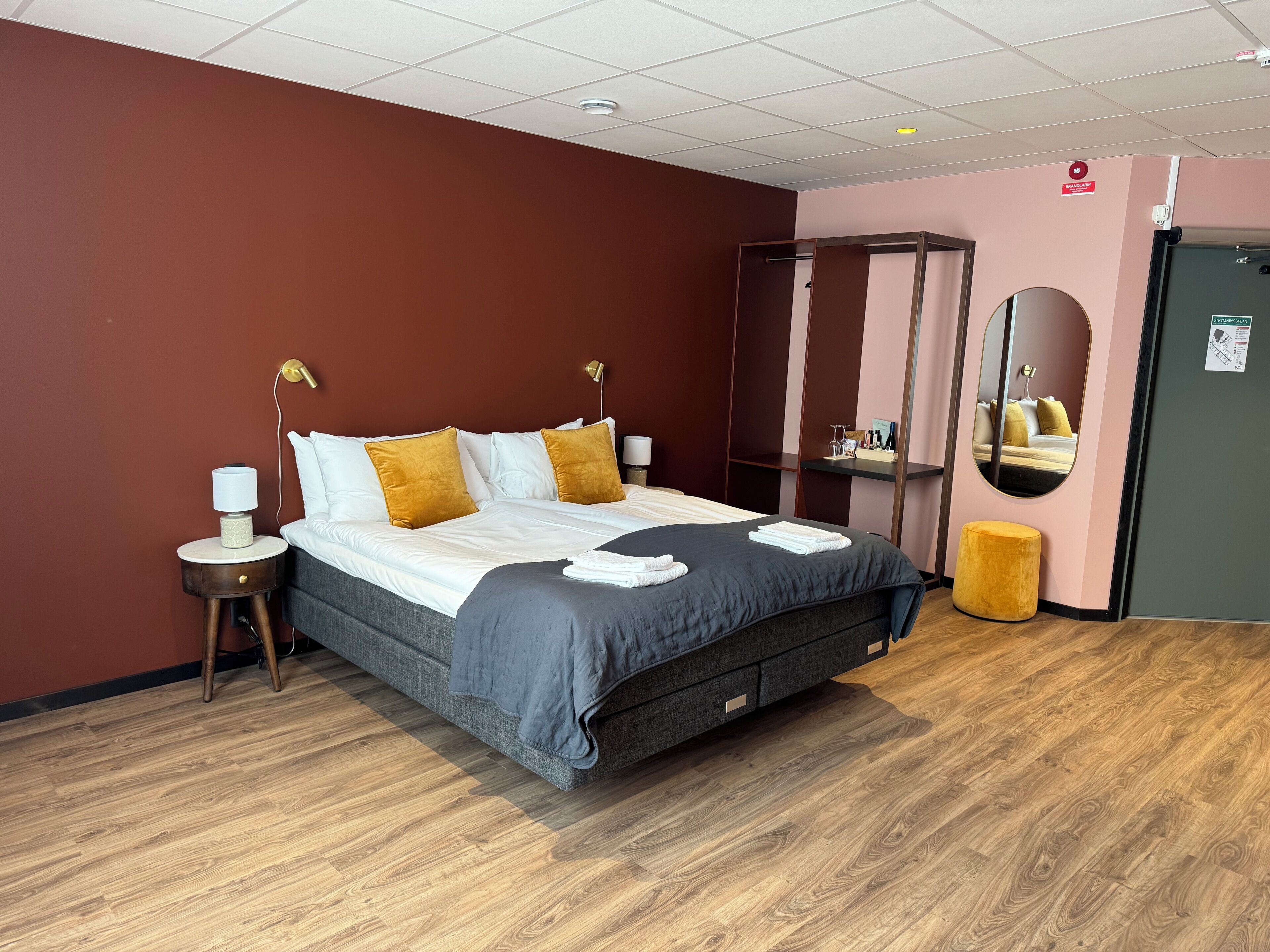 A hotel room with a bed, bedside tables, a mirror, and a wardrobe.