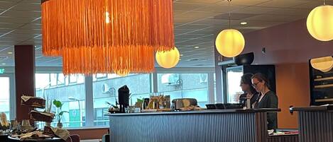 Un interior moderno con una mesa redonda de madera, una zona de bar y lámparas colgantes color naranja.