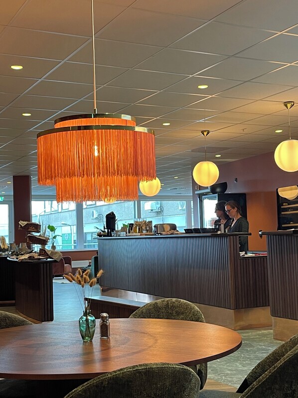 A modern interior with a round wooden table, a bar area, and hanging orange chandeliers. - Hotell Sillen (Lysekil)