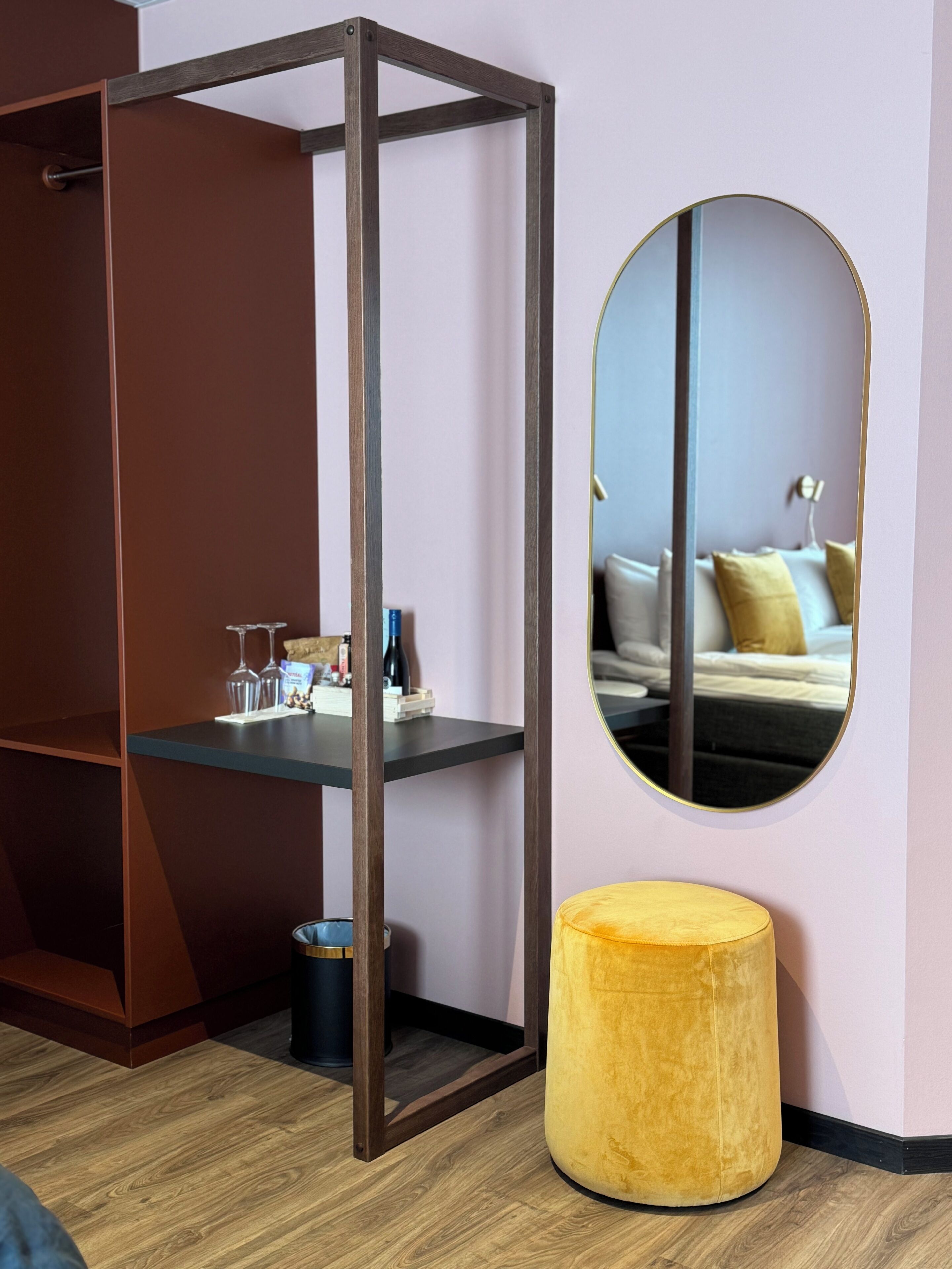 A room with a wooden wardrobe, a round mirror, and a yellow ottoman.