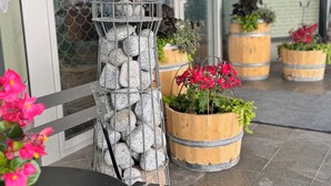 A patio area with a metal sculpture, wooden barrels with plants, and a black table. - Hotell Sillen (Lysekil)