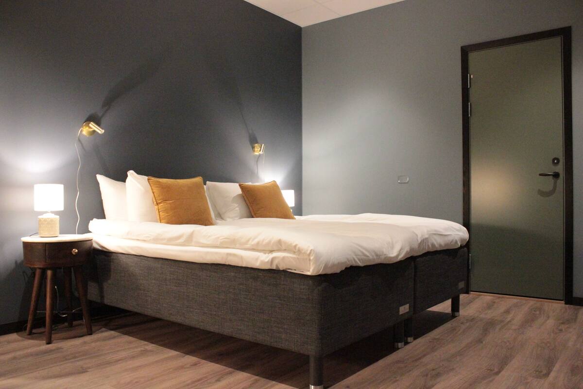 A modern bedroom with a large bed, a nightstand, and a door.