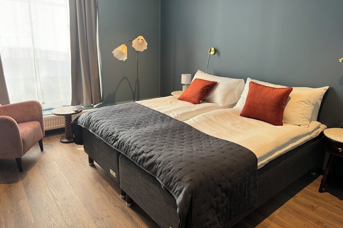 A modern hotel room with a large bed, a bedside table, a chair, and a floor lamp.