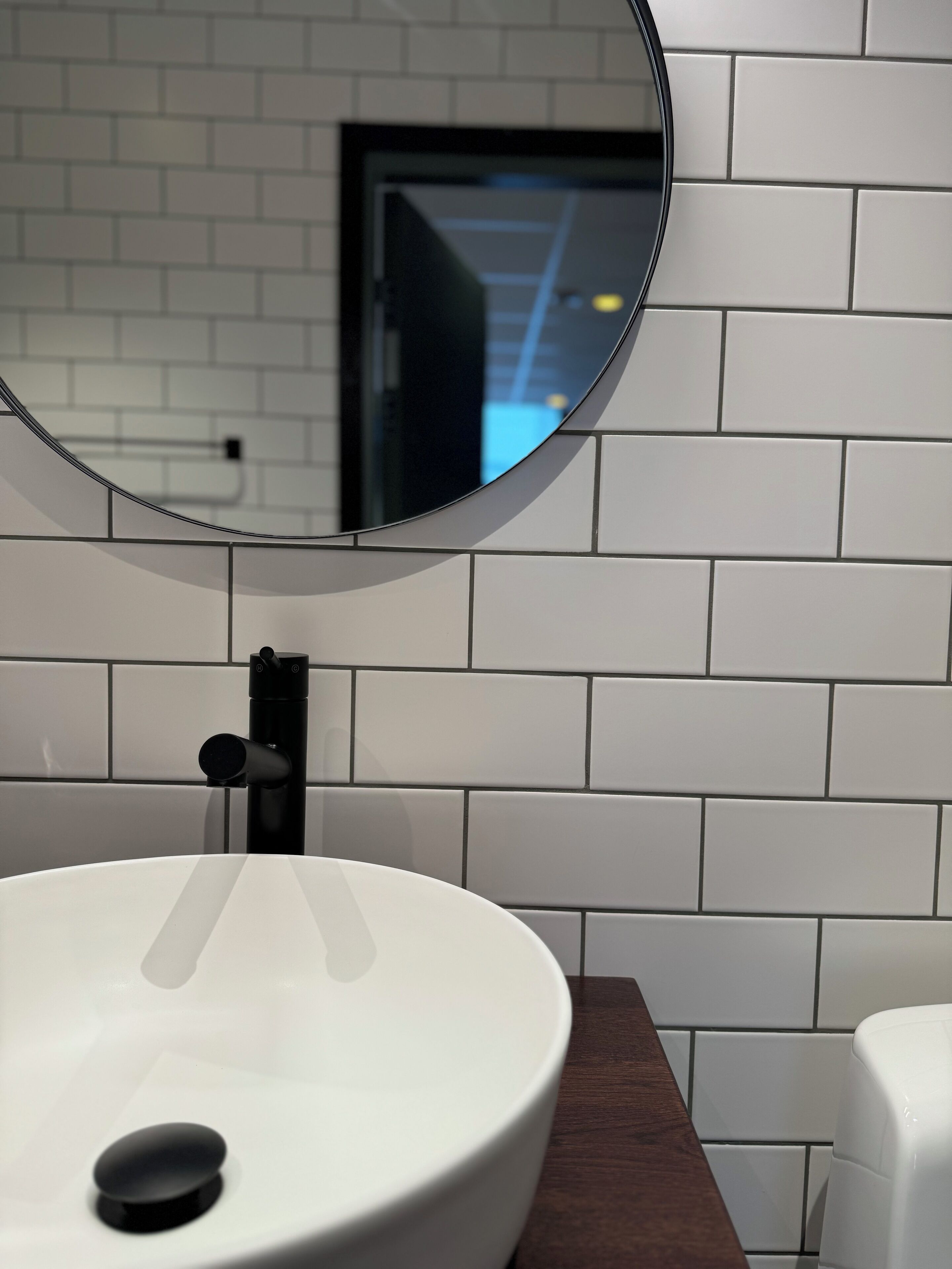 A bathroom with a white sink, a round mirror, and a wooden countertop.