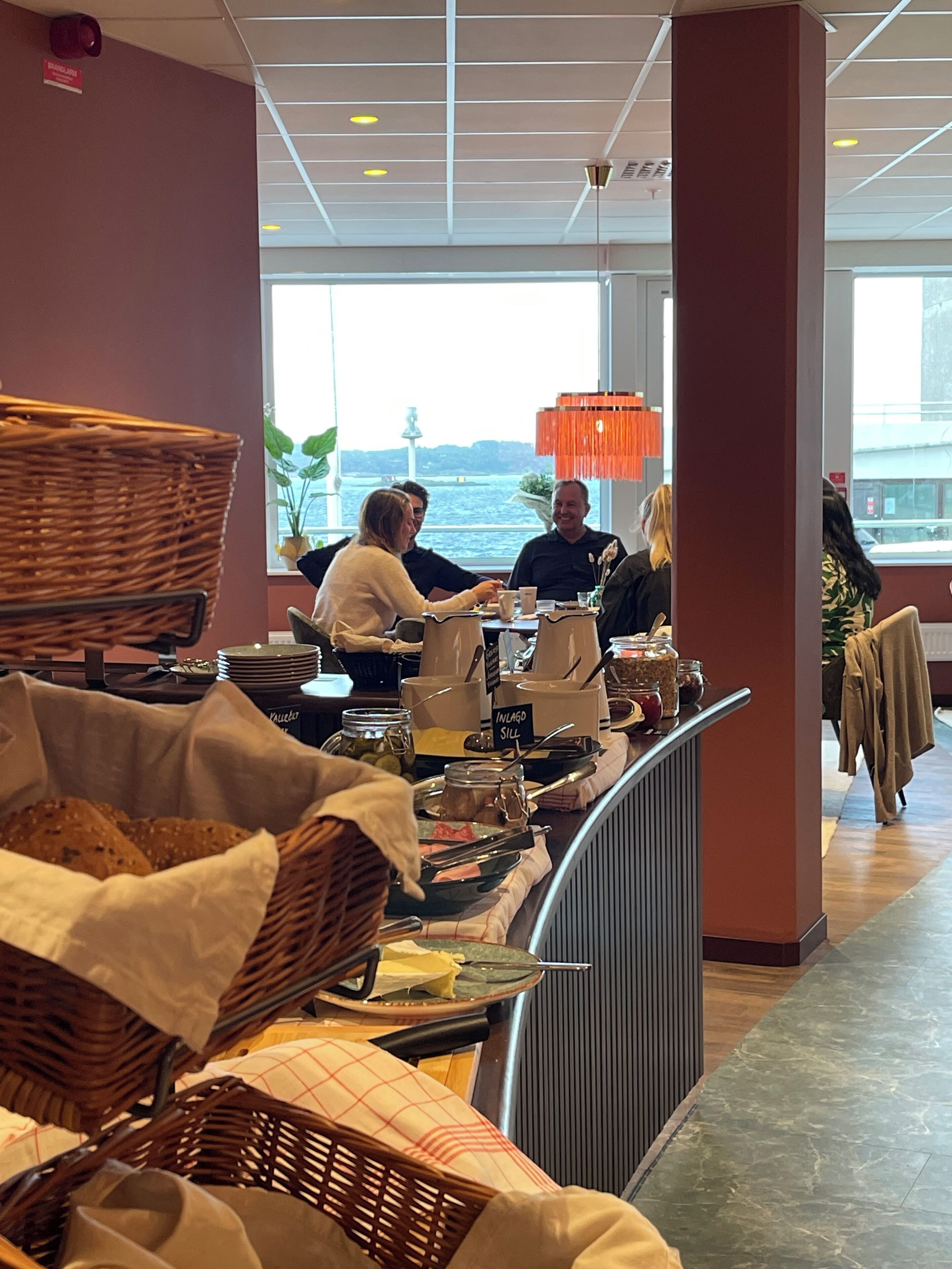 A buffet area with wicker baskets, a sign reading "In Lago Sill," and a view of the water outside.