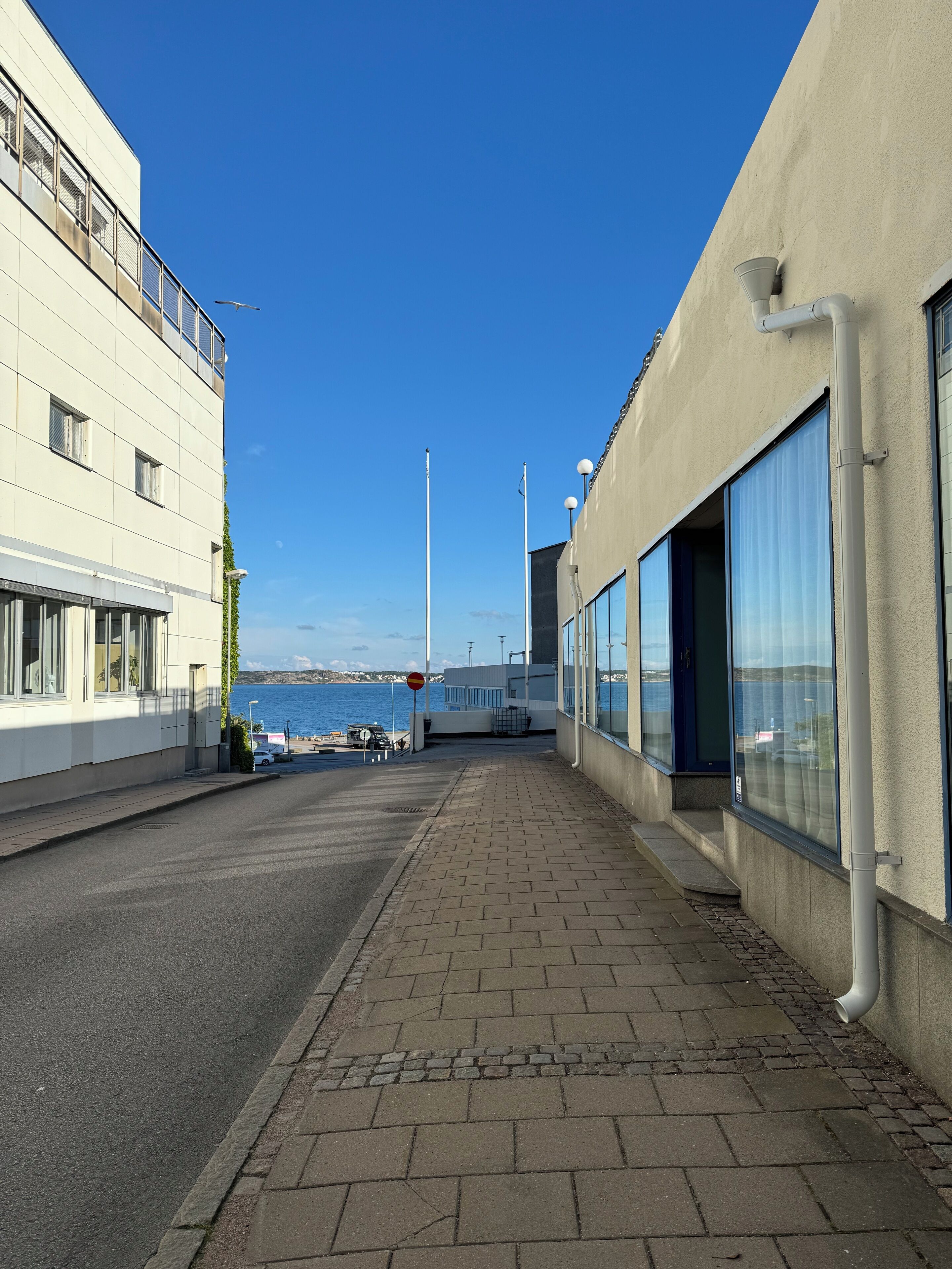 En byggnad vid kusten med stora fönster som vetter mot havet, en stenlagd gångväg och fri utsikt över vattnet.