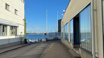 En byggnad vid kusten med stora fönster som vetter mot havet, en stenlagd gångväg och fri utsikt över vattnet.