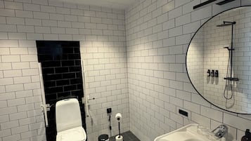 Un baño moderno con azulejos blancos tipo metro, un inodoro negro, un lavamanos blanco y una ducha con un espejo circular.