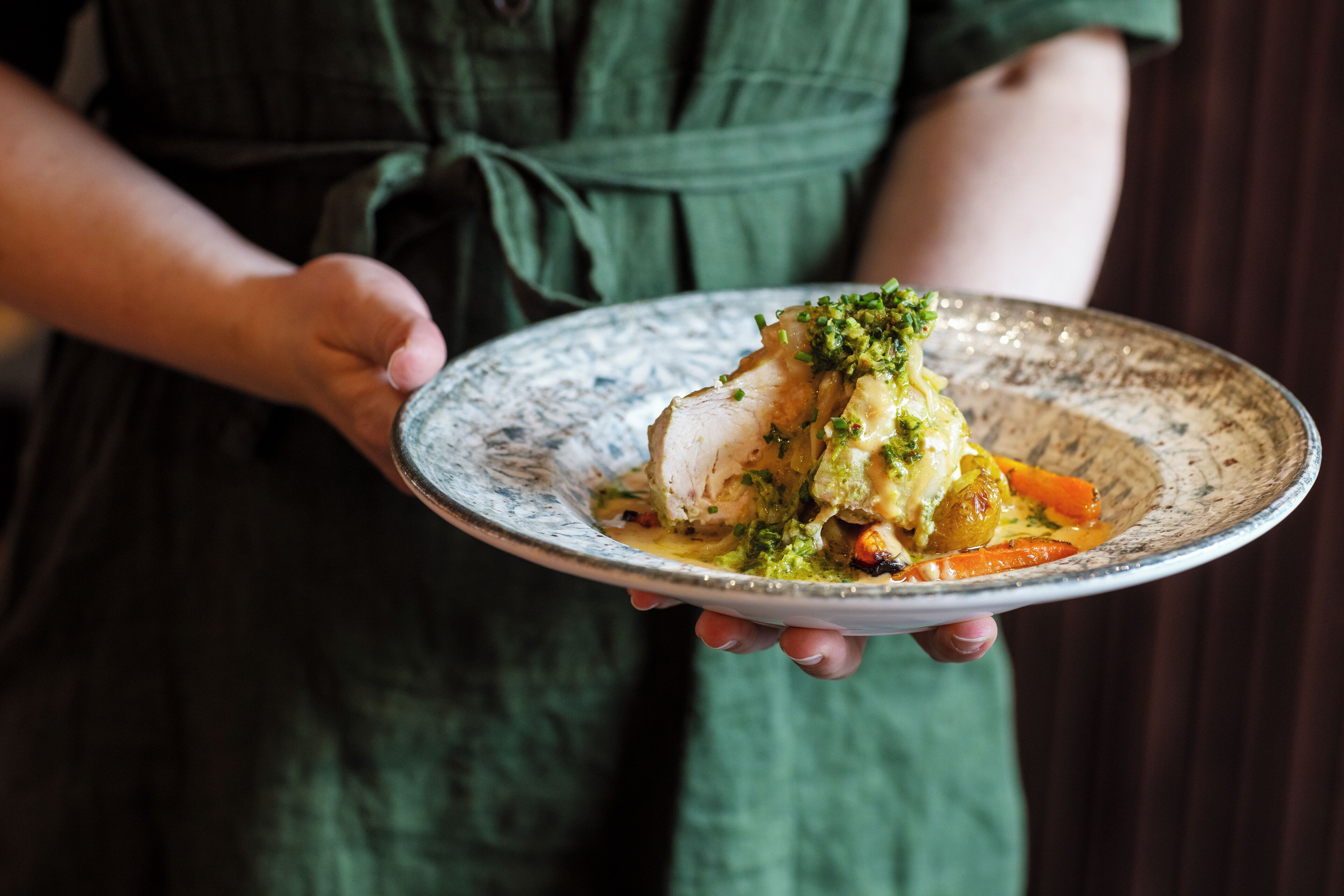 A person holding a plate with a dish that includes fish, vegetables, and a green garnish.