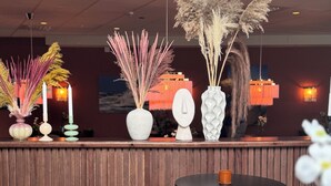 A reception area with a wooden counter, two yellow cushioned chairs, a round table with a cup, and decorative vases with plants. - Hotell Sillen (Lysekil)