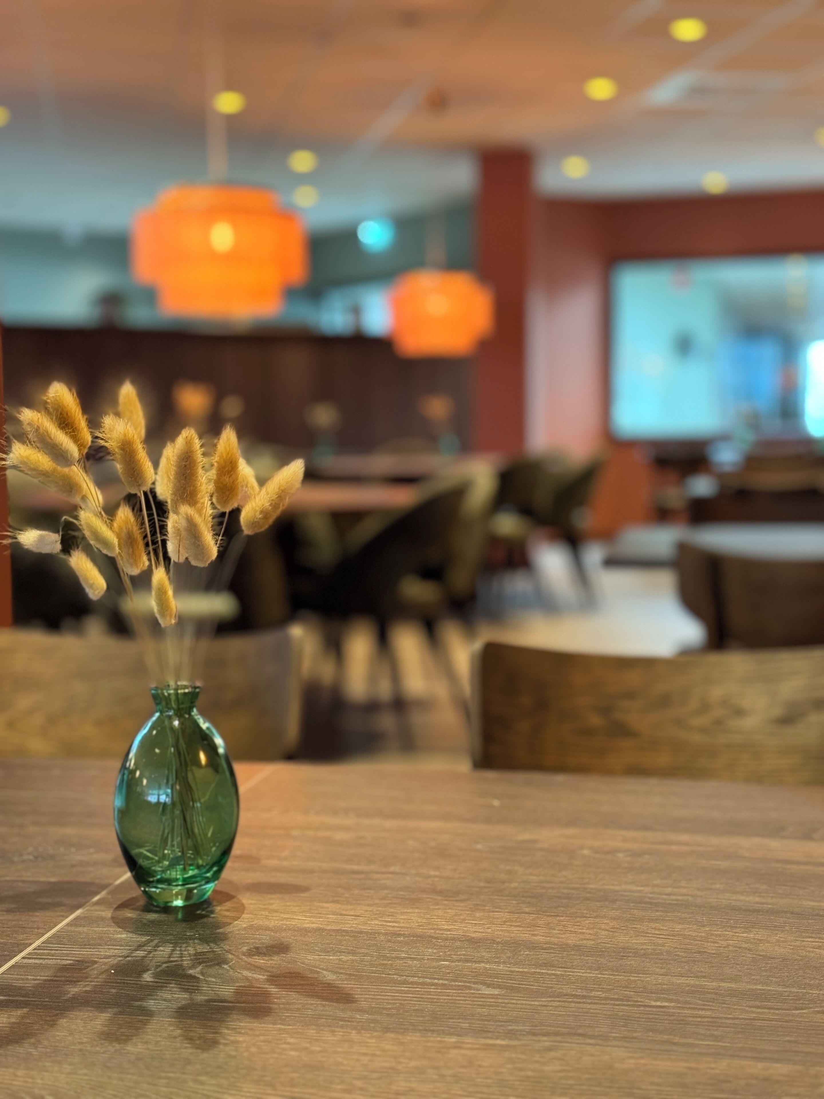 A green vase with dried plants on a wooden table in a restaurant setting.