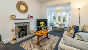 A living room with a fireplace, a television, a dining area with chairs, and a sofa. - Stunning Home Next to Nottingham University | Off-Street Parking | Sleeps 8  (Beeston)