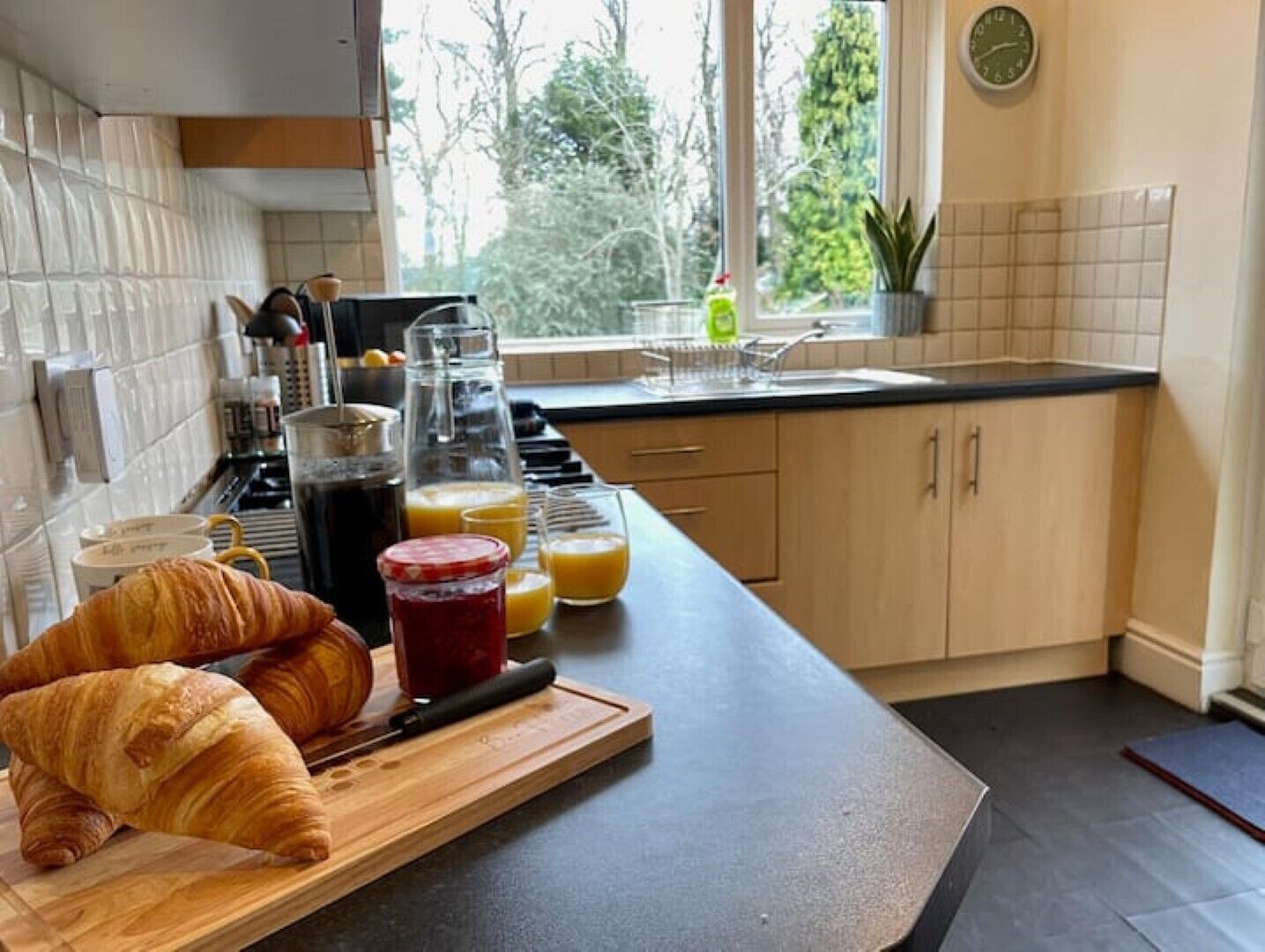 A kitchen with a wooden countertop, a window with a view of trees, and a clock on the wall.