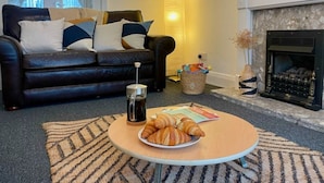 A living room with a black leather sofa, a coffee table with croissants, a fireplace, and a lamp. - Stunning Home Next to Nottingham University | Off-Street Parking | Sleeps 8  (Beeston)