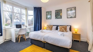 A hotel room with a large bed, a desk, and a computer. There are three framed pictures on the wall and a lamp on the nightstand. - Stunning Home Next to Nottingham University | Off-Street Parking | Sleeps 8  (Beeston)