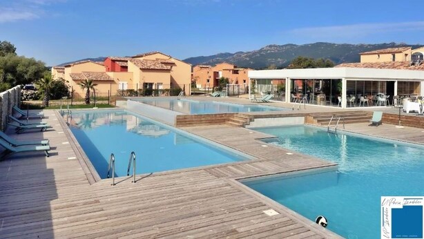 A pool area with wooden decking, lounge chairs, and a view of buildings and hills in the background. - villa Suera - 2 Bedrooms - Pools - Air Conditioning (Lecci)