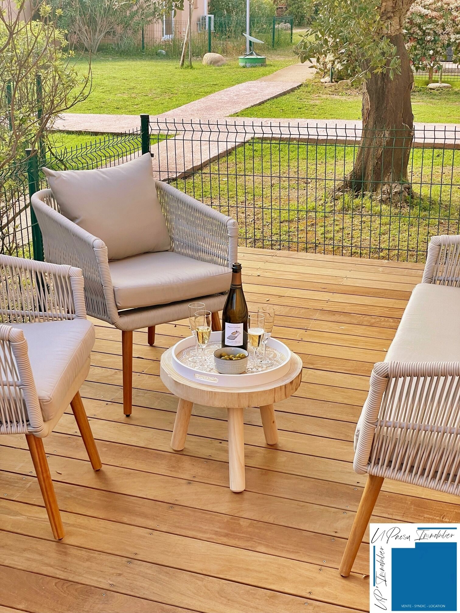 A deck with wicker chairs and a small round table with a bottle and glasses.