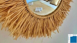 A circular mirror with a straw-like frame, reflecting a bedroom with a bed, pillows, and a wall decoration. - villa Suera - 2 Bedrooms - Pools - Air Conditioning (Lecci)
