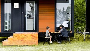 A modern, compact building with a black exterior and wooden accents, featuring a small outdoor seating area with a table and chairs. - Forest View Cottage 1 (森林景觀度假小屋1) (Jiaoxi Township)