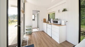 Une cuisine de taille réduite, dotée de meubles blancs, d’un plan de travail en bois et d’une fenêtre donnant sur un paysage naturel.