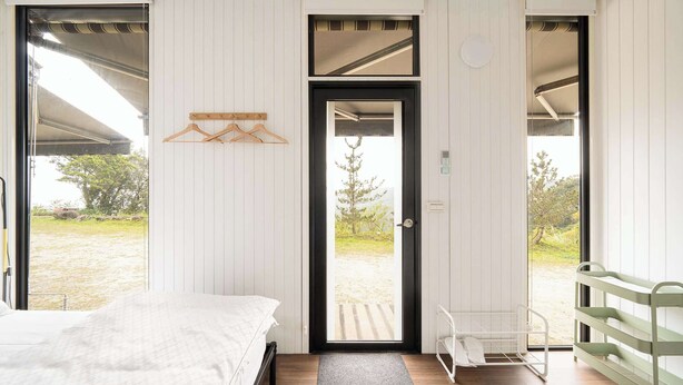 Une chambre à coucher avec un lit, une porte donnant sur l’extérieur, un porte-manteau mural et une fenêtre offrant une vue sur le paysage.