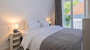A neatly arranged bedroom with a bed, bedside lamps, and a window with curtains. - Atlantic Grand Hotel - Appartement (Lübeck)