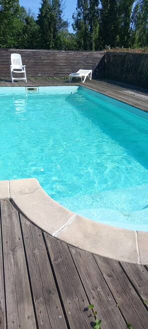 A swimming pool with a wooden deck and two white lounge chairs.
