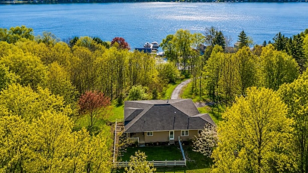 A house with a sloped roof, surrounded by lush green trees and a lake.