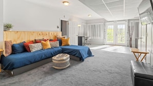 A spacious living room with a large blue sofa, a wooden headboard, and a grey carpet.