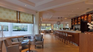 Un amplio bar con una barra larga, varios taburetes y vistas al exterior a través de grandes ventanales.