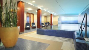 Un vestíbulo de hotel con una planta grande en maceta, una recepción y una zona de estar con sillones reclinables.