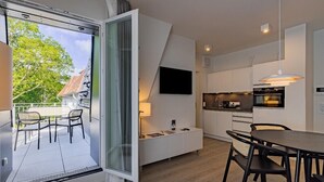 Una cocina moderna con comedor, un televisor en la pared y un ventanal corredero que da a un balcón.