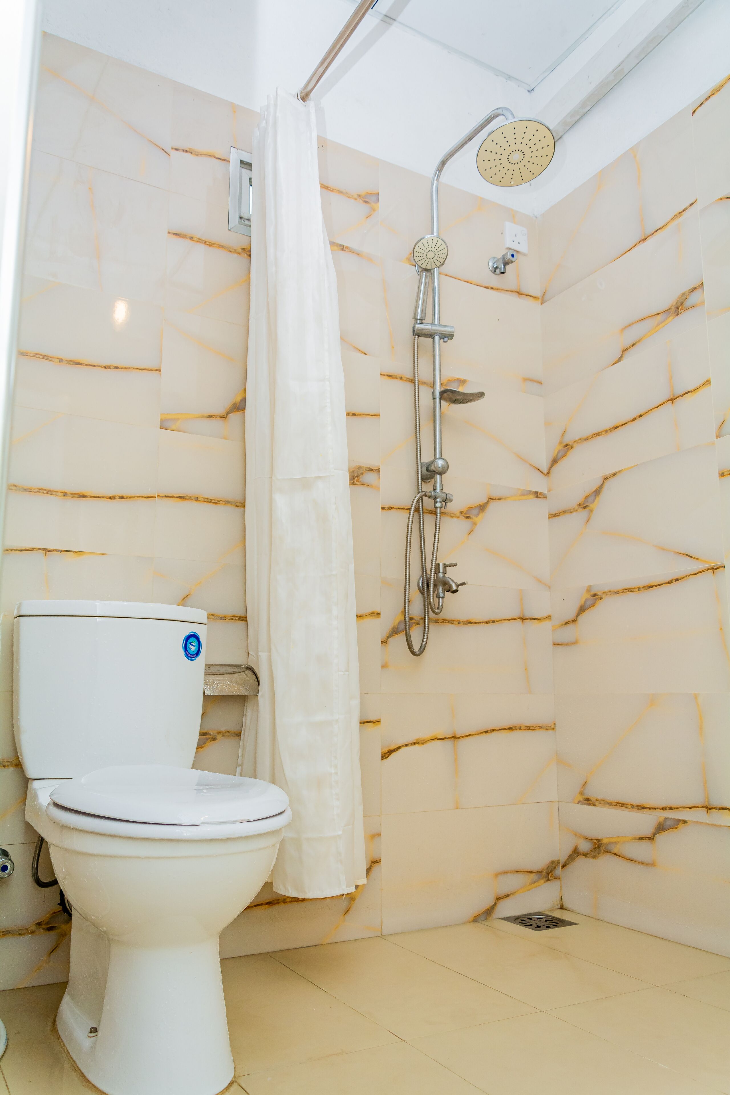 A bathroom with a toilet, a shower with a handheld showerhead, and marble-patterned walls.