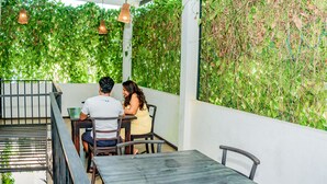 A covered outdoor seating area with tables and chairs, surrounded by lush green foliage and hanging pendant lights. - ShiCo Transit Hotel (Seeduwa - Katunayake)