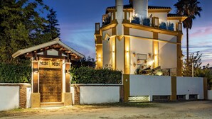 Um edifício com um grande portão de madeira, fachada branca e varanda com vasos de plantas.