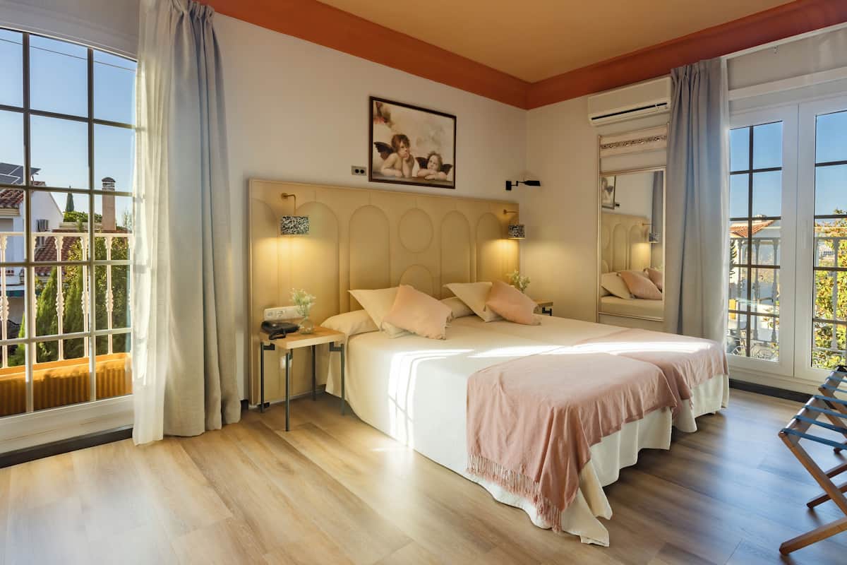 Un dormitorio con una cama grande, mesitas de noche, un velador, una ventana con cortinas y un cuadro en la pared.