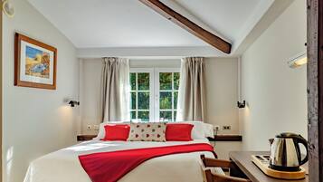 A bedroom with a bed, a window, a desk with a kettle, and a chair.
