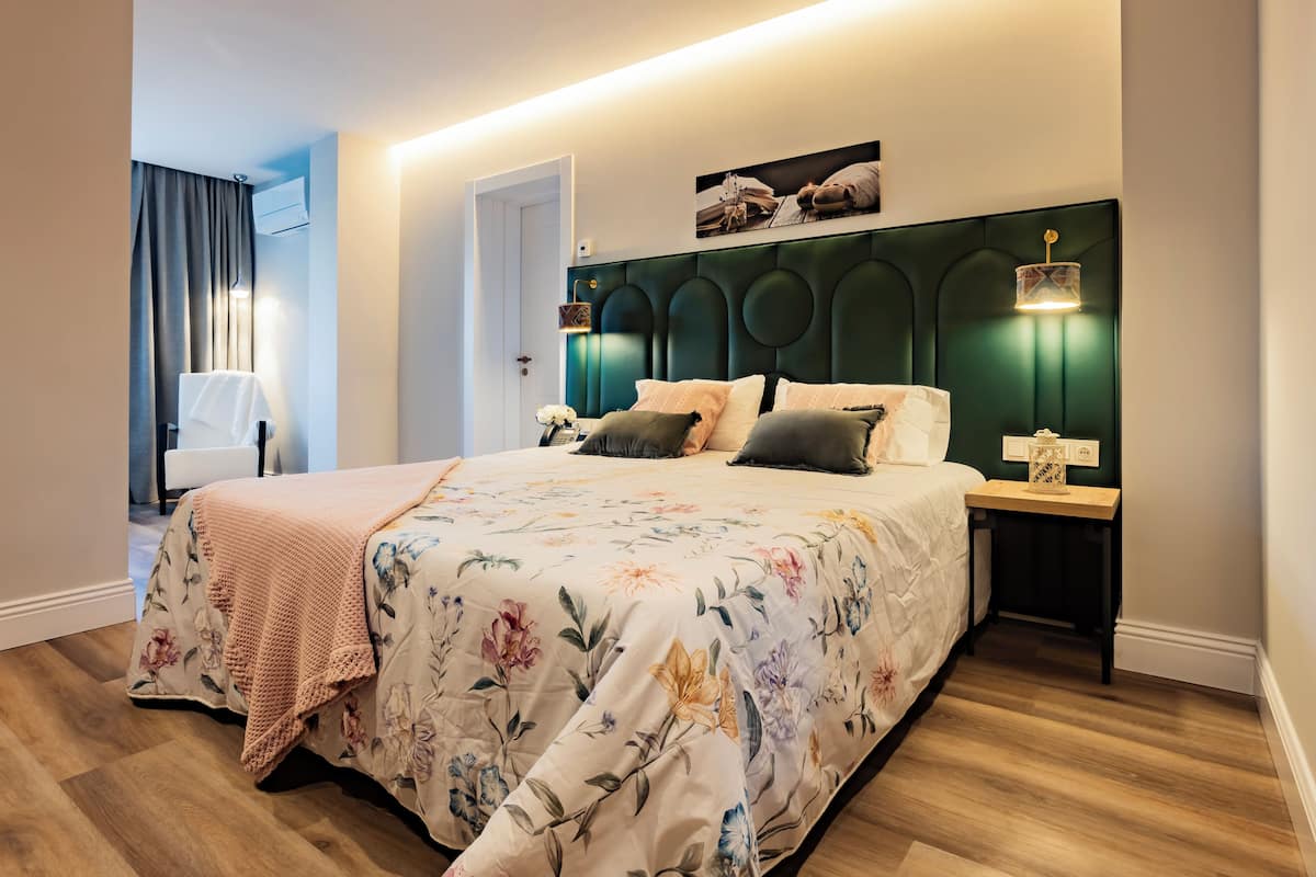 Un dormitorio con colcha estampada, cabecero verde, lámparas de noche y suelo de madera.