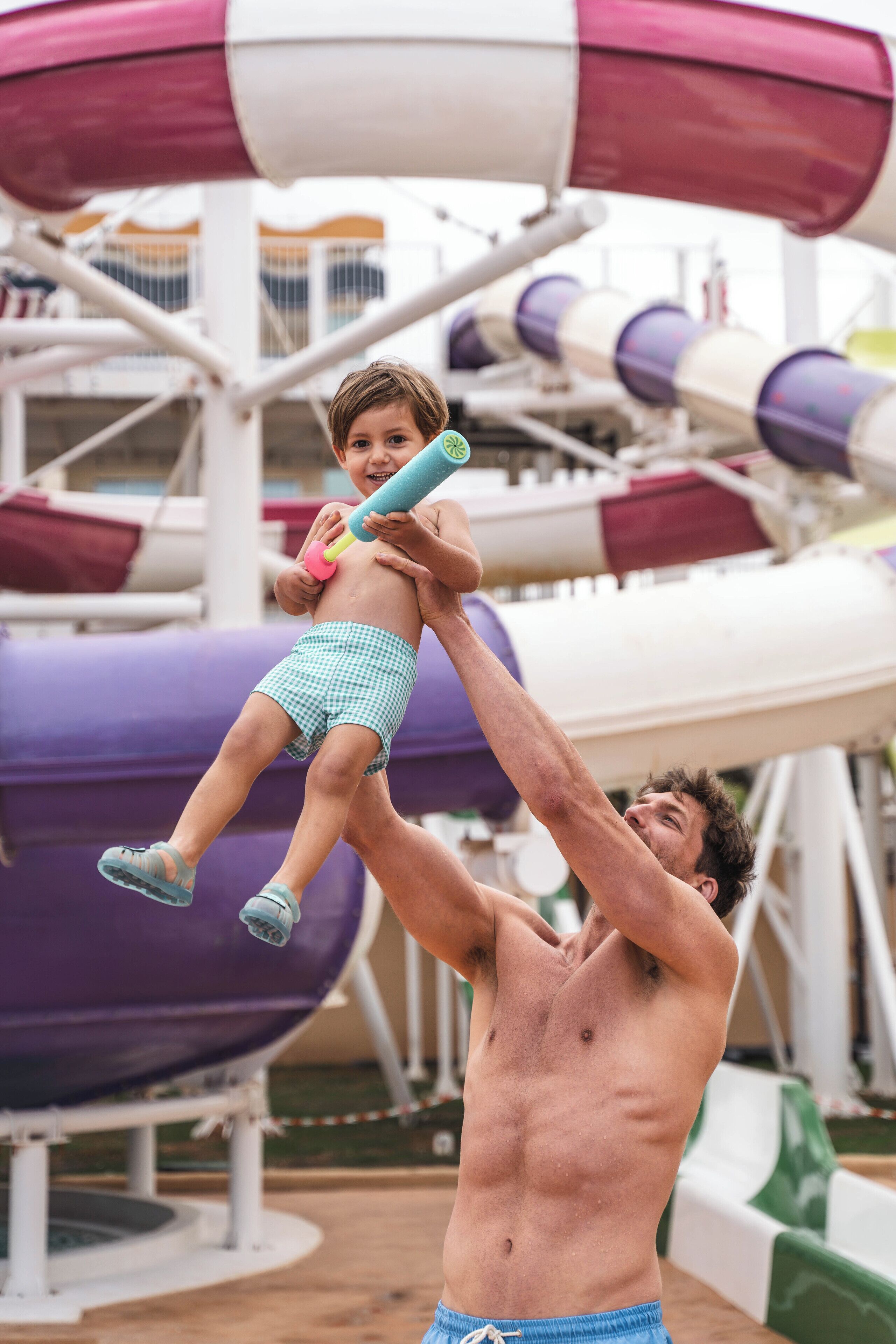 Un homme porte un enfant devant une structure de toboggan aquatique.