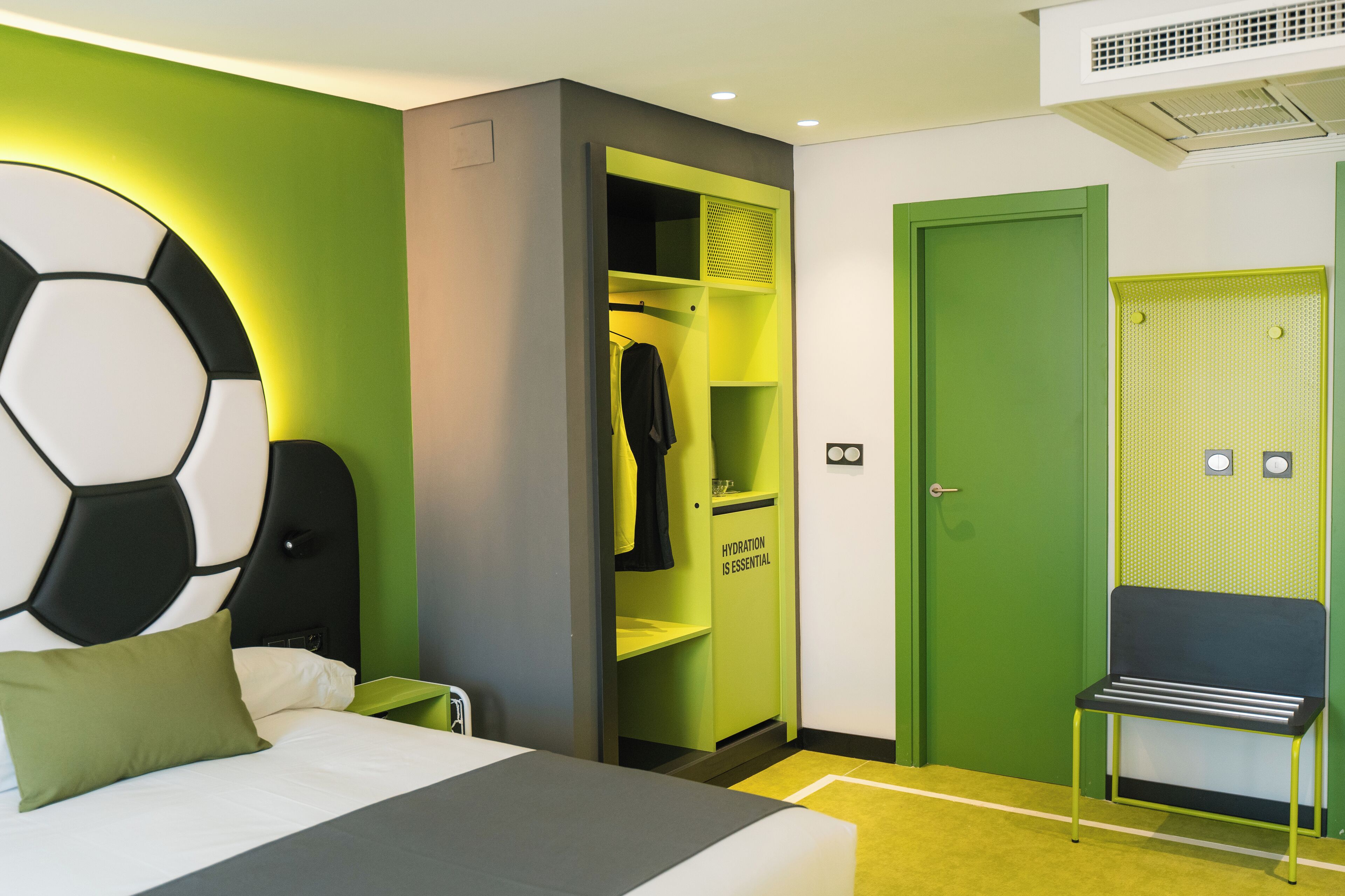 Habitación de hotel con cama, pared verde, armario con letrero de hidratación y puerta verde.