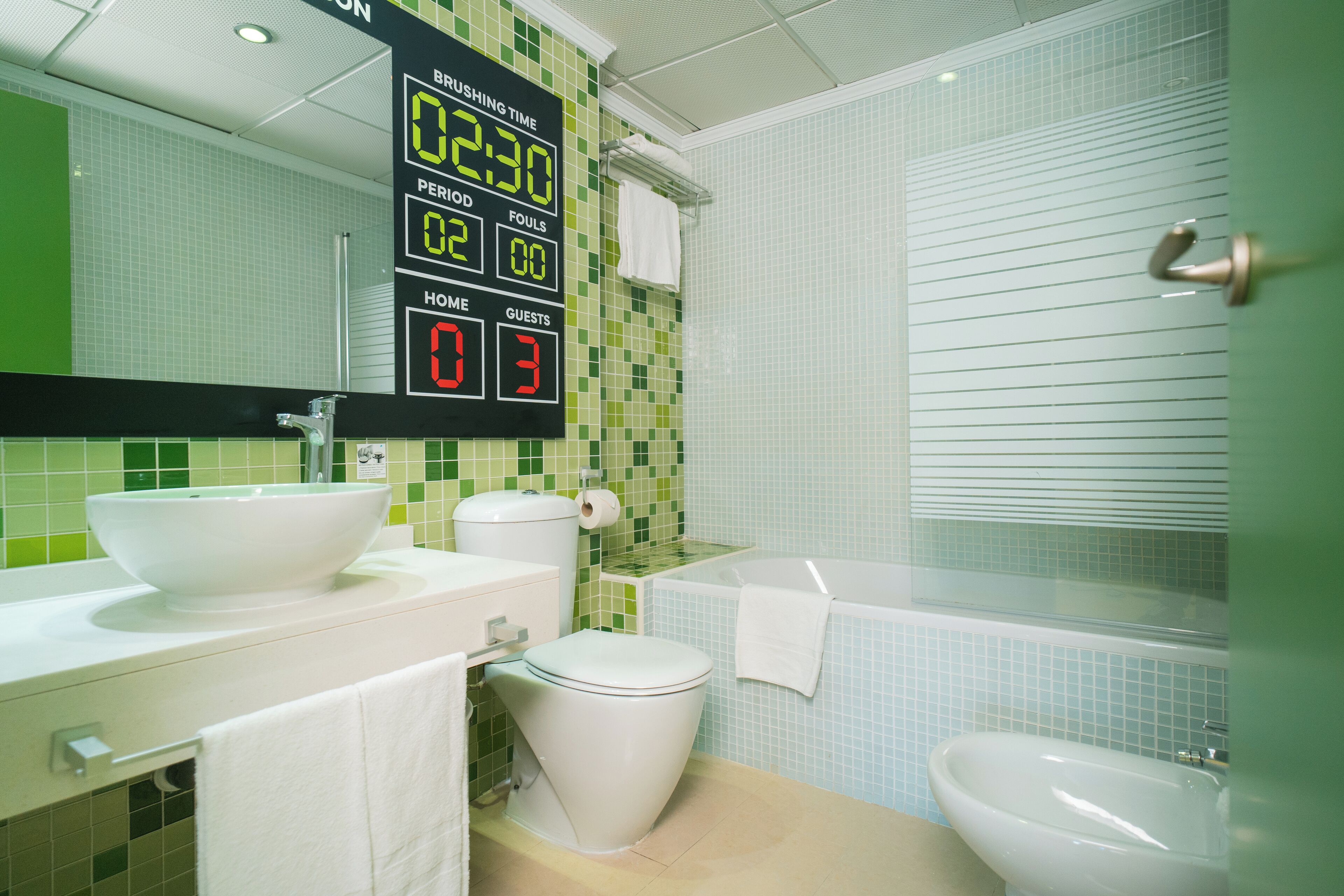 Une salle de bain équipée d’un écran numérique affichant l’heure, le quart-temps, les fautes, le score de l’équipe à domicile et celui de l’équipe visiteuse.