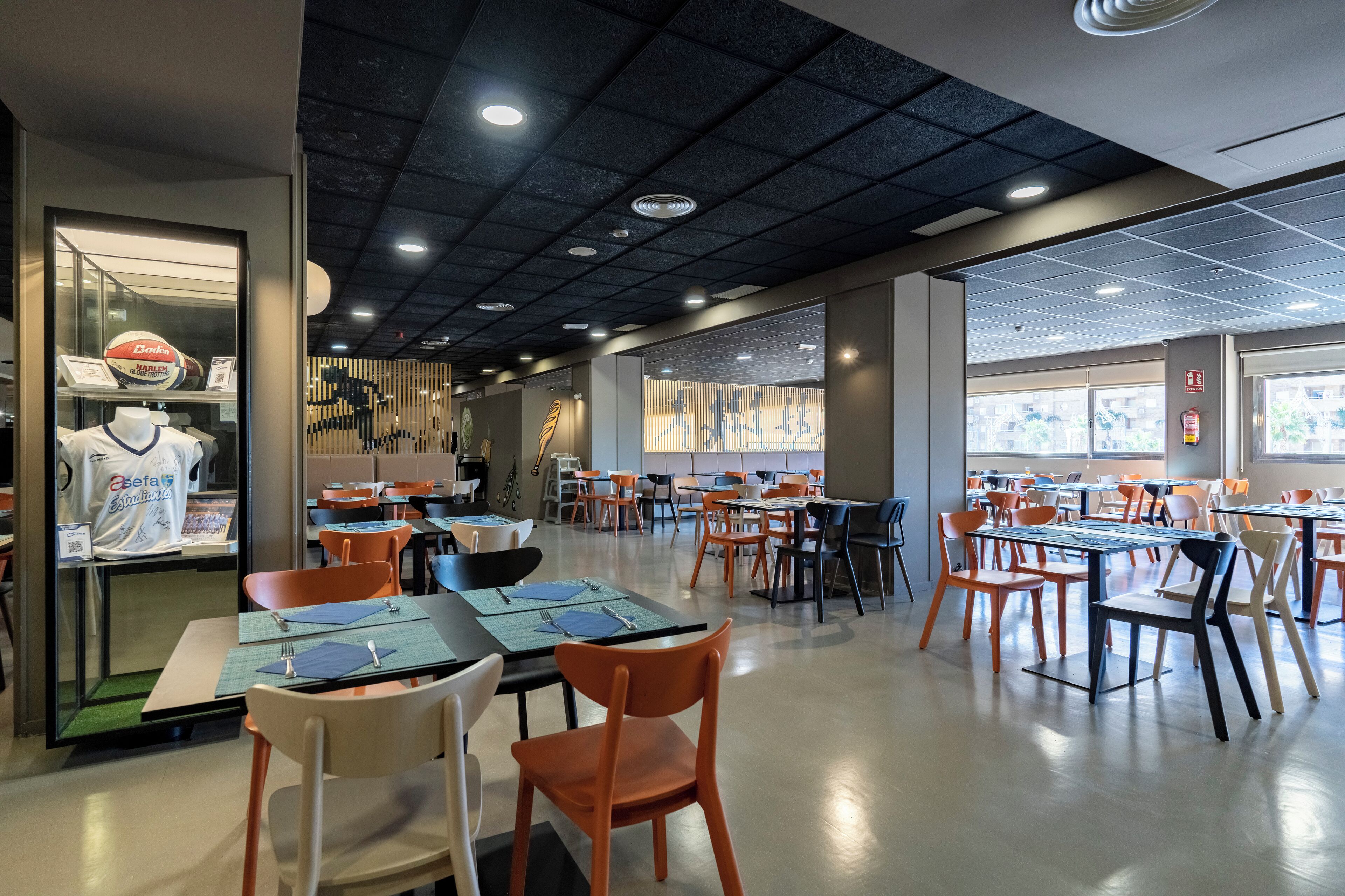 En moderne restaurant med borde og stole, en udstillingsdisk med mad og et loft med indbyggede lys.