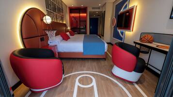 A hotel room with a basketball theme, including a bed with a net, a basketball hoop, and a basketball on the nightstand.
