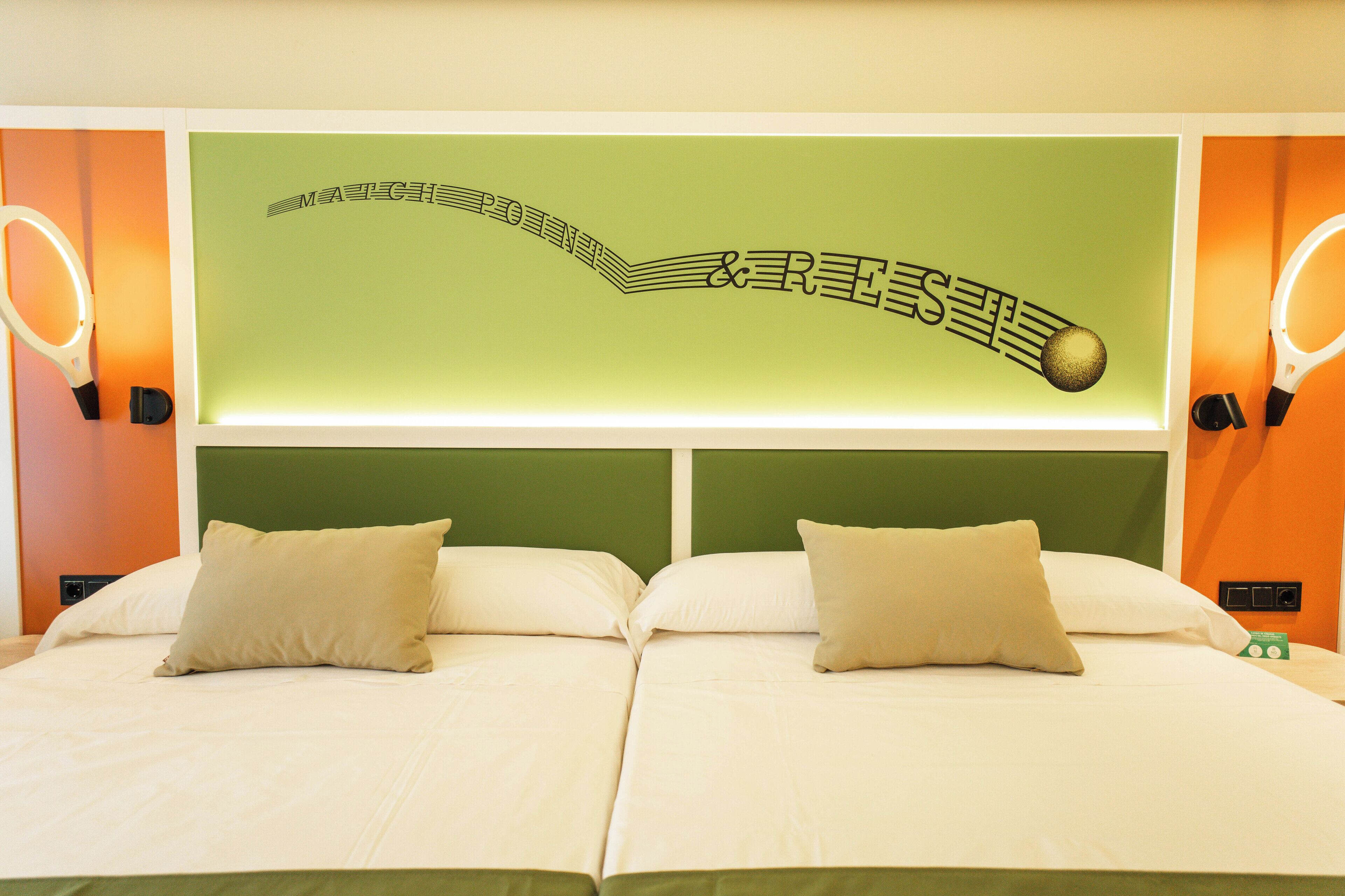 Habitación de hotel con cama, dos almohadas, pared verde con diseño de nota musical y dos luces de pared.