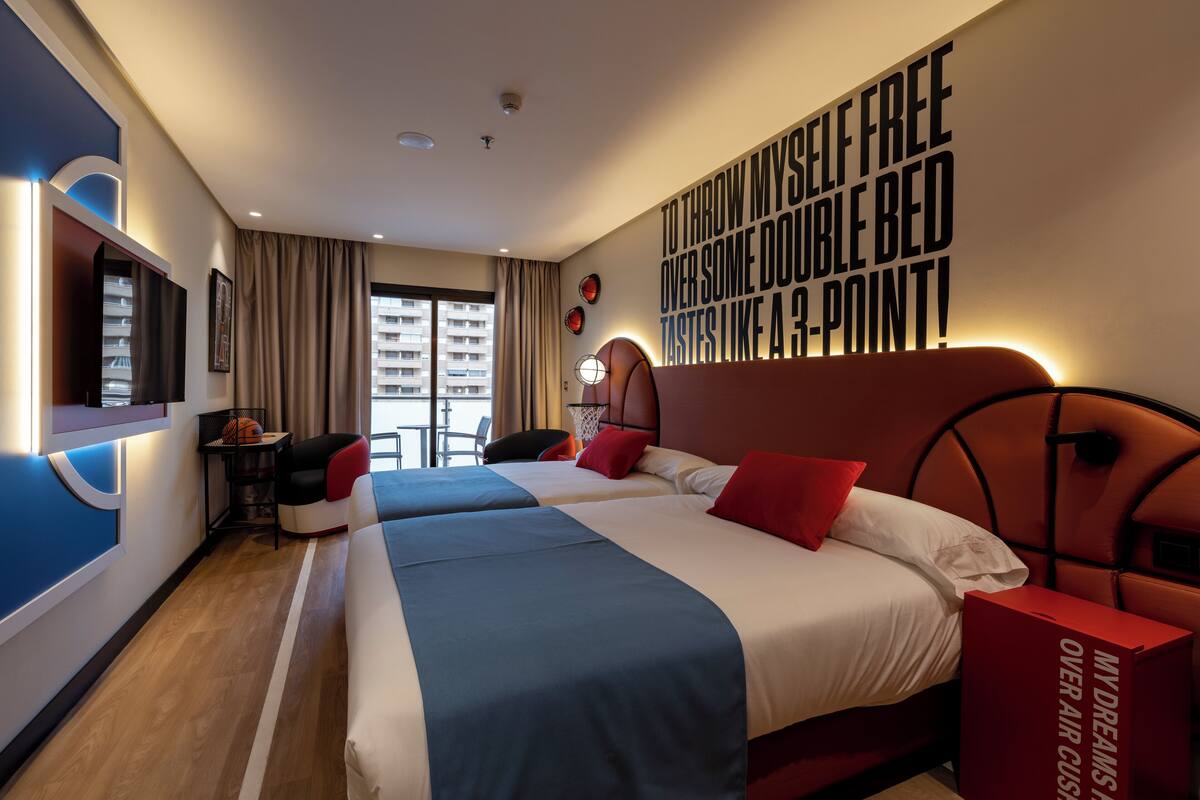A hotel room with two beds, a large window, and a wall with motivational text.