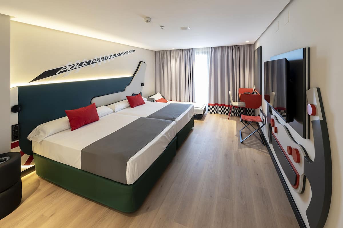 A modern hotel room with a large bed, a desk with a chair, a TV, and a window with curtains.