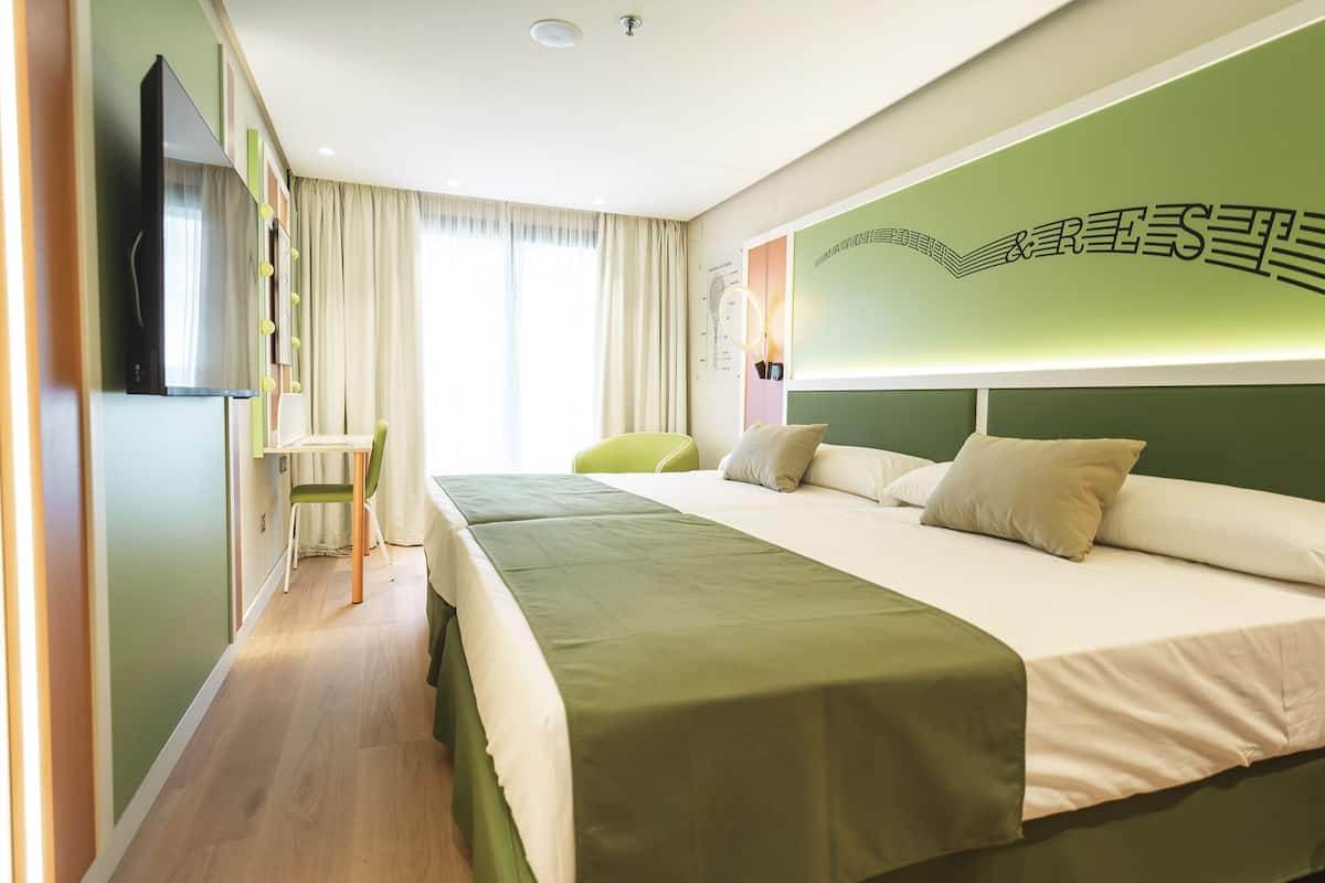 A hotel room with a bed, a desk, a chair, a TV, and a wall with a decorative design.