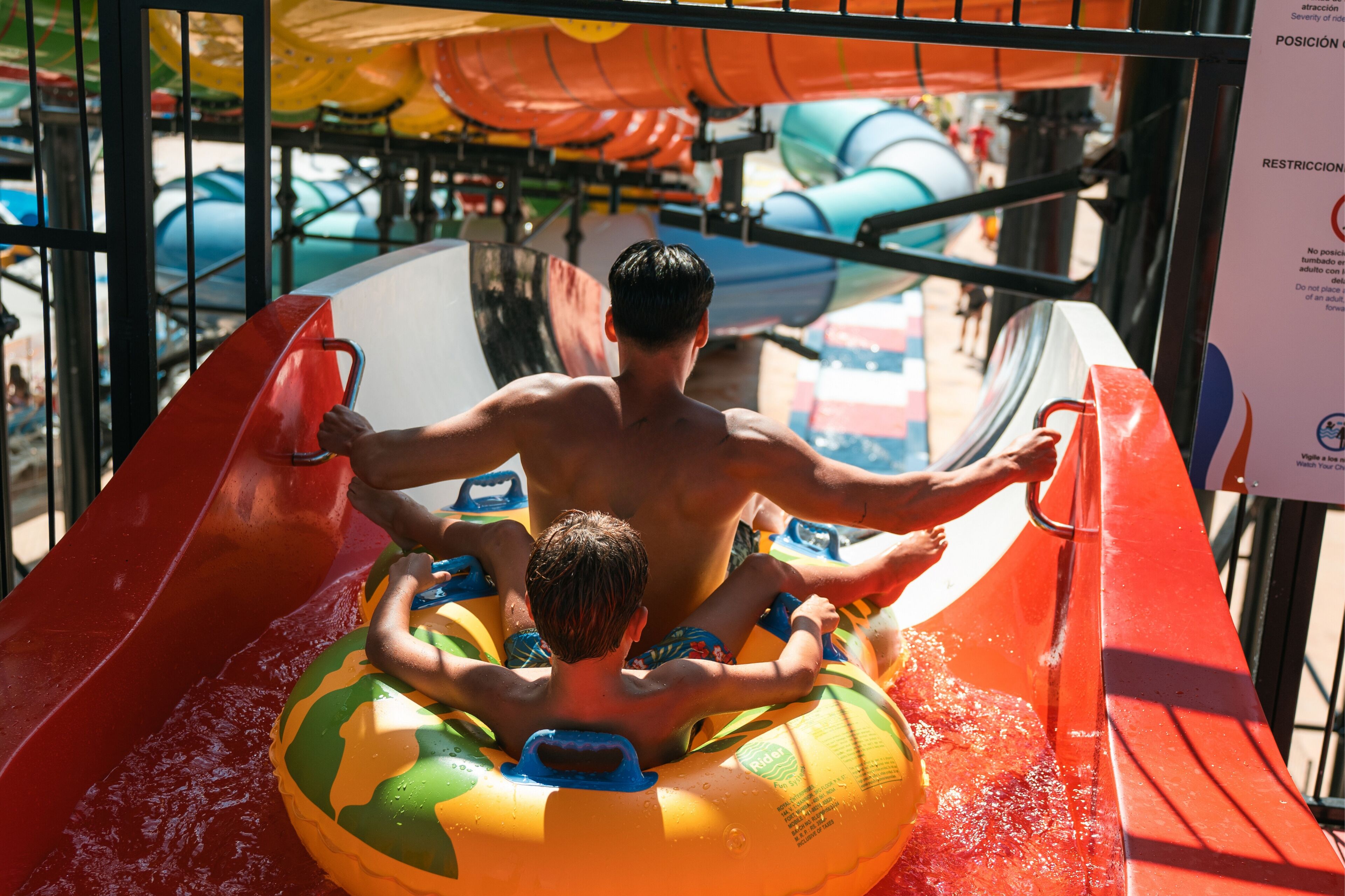 A water slide with a person and a child in an inflatable raft.