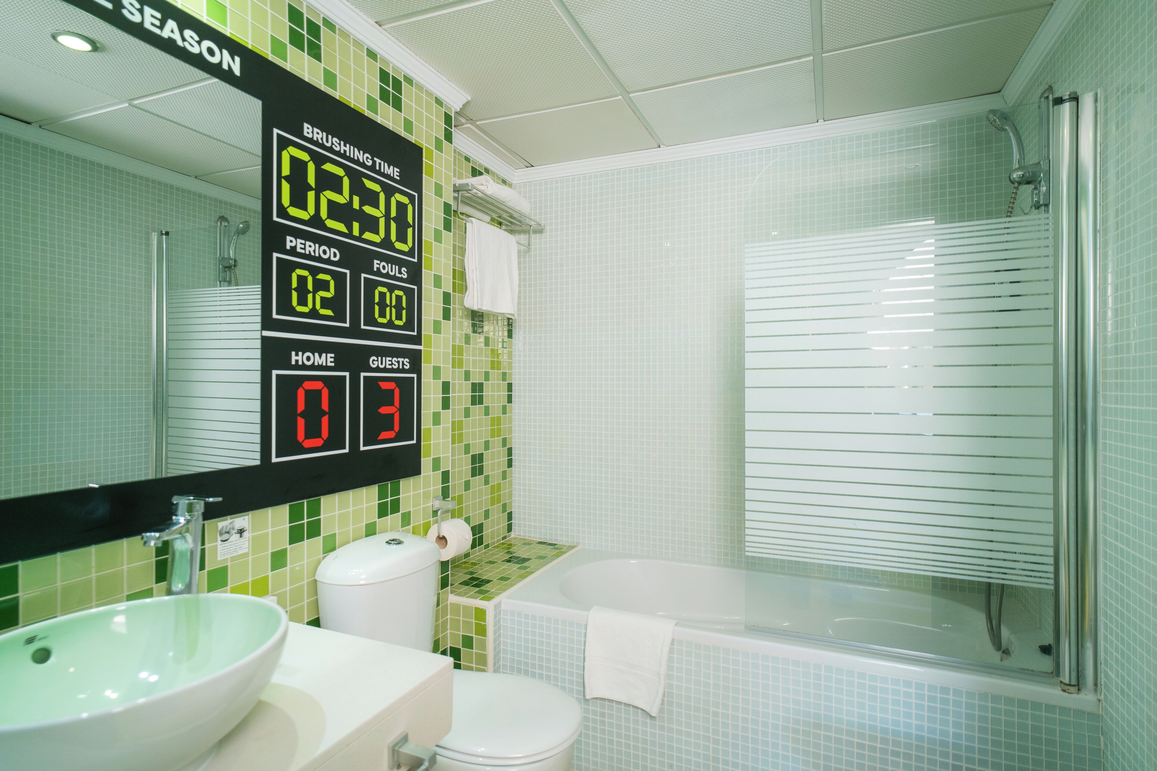 A bathroom with a digital clock displaying the time, a sink, toilet, and a bathtub.