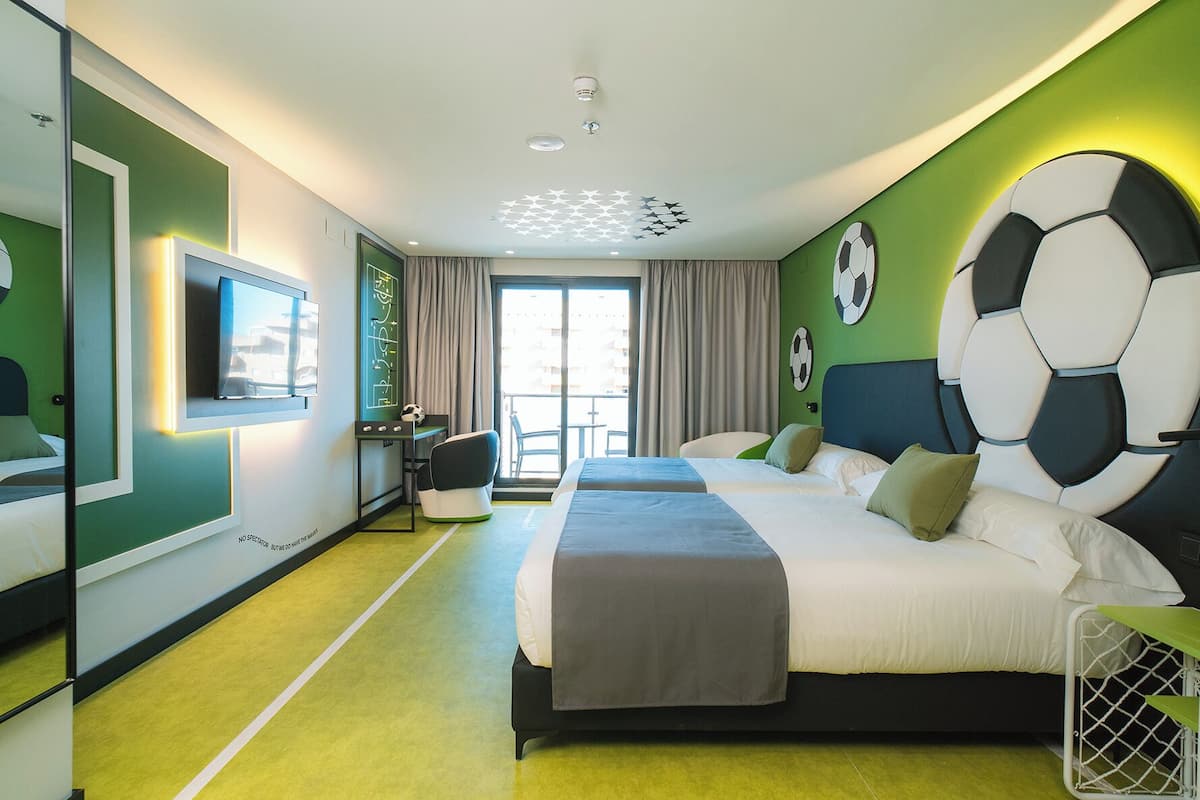 A hotel room with a large bed, a desk, a chair, a TV, and a window with curtains.